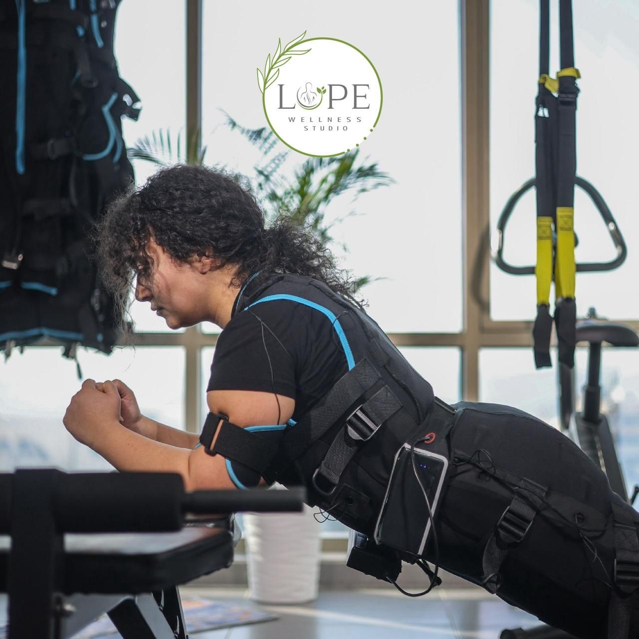 Person in fitness attire performing a plank exercise at a wellness studio with exercise equipment in the background.